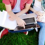 Young happy students with laptop, books and notes outdoors.